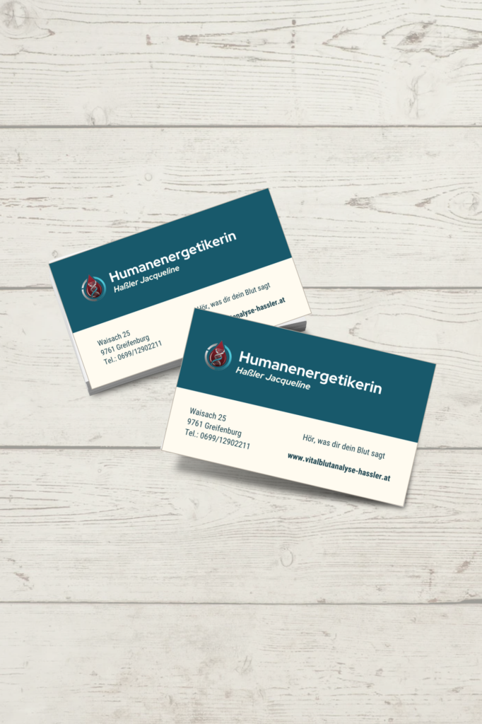 1. Alt-Text Zwei Visitenkarten für die Humanenergetikerin Jacqueline Haßler, versetzt auf einem hellen Holzhintergrund liegend. Das Design ist horizontal in eine dunkelblaue obere Hälfte und eine cremeweiße untere Hälfte geteilt.