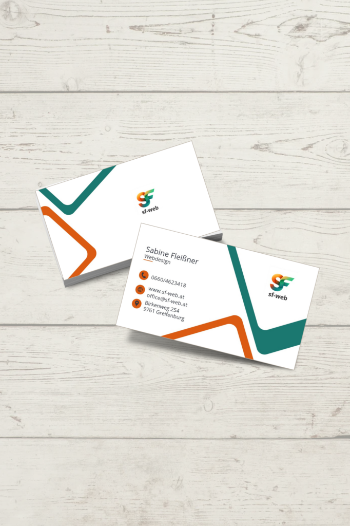 Zwei moderne, weiße Visitenkarten von sf-web (Sabine Fleißner), die versetzt auf einem hellen Holzhintergrund liegen. Das Design besticht durch dynamische, winkelförmige Grafikelemente in Türkis und Orange sowie ein buntes Logo.