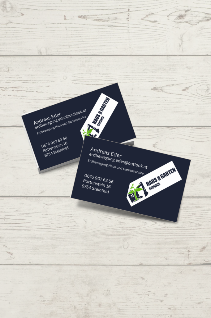 Zwei dunkelblaue Visitenkarten für „Haus und Garten Service“ von Andreas Eder, versetzt angeordnet auf einer hellen Holzoberfläche. Das Design kombiniert weiße Textelemente mit einem auffälligen Logo, das einen Bagger und eine Pflanze zeigt.