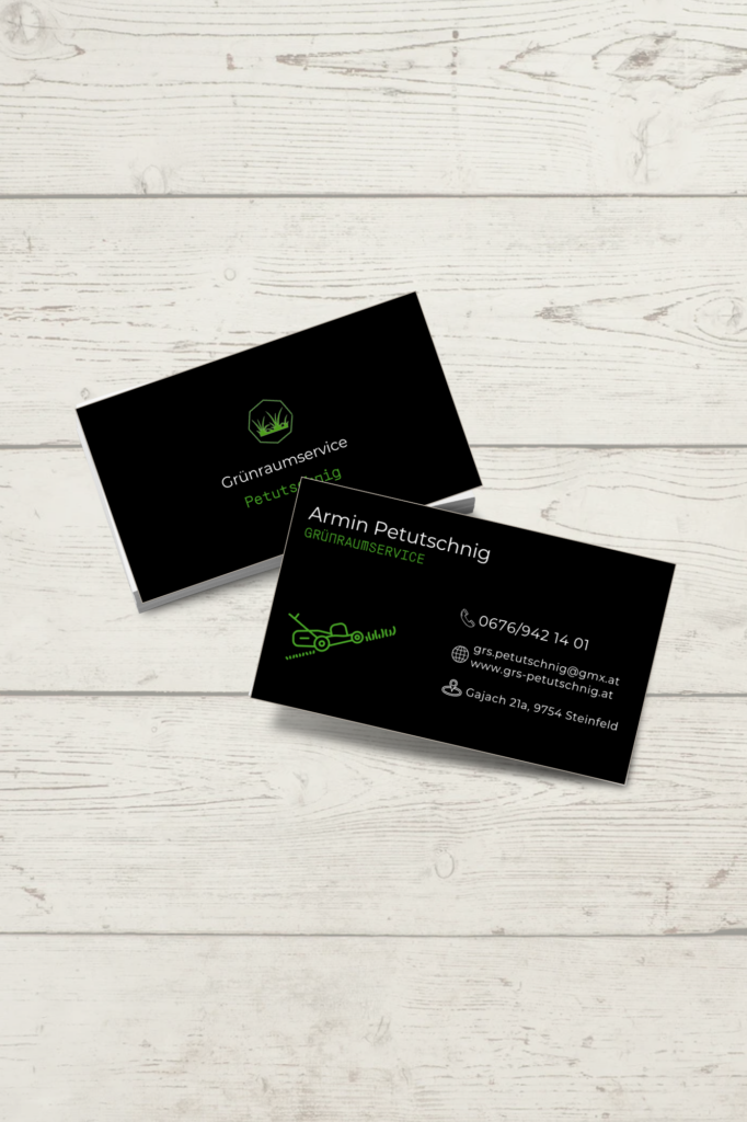 Mockup von zwei schwarzen Visitenkarten für „Grünraumservice Petutschnig“, die versetzt auf einem hellen Holzhintergrund liegen. Die Karten zeigen ein grünes Logo mit Rasen-Motiv sowie Kontaktdaten in weißer und grüner Schrift.